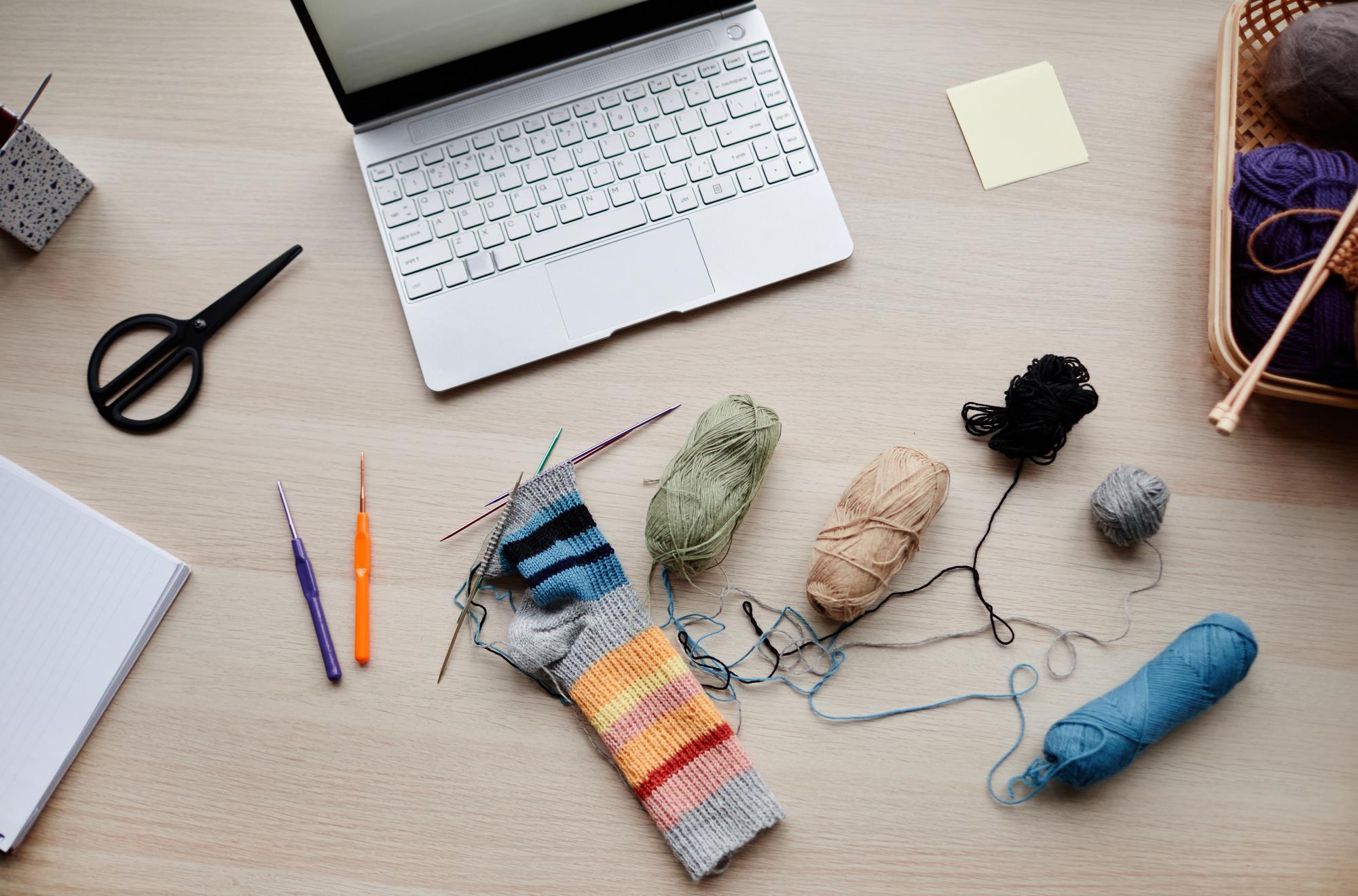 workspace with threads, needles and a laptop showing pattern